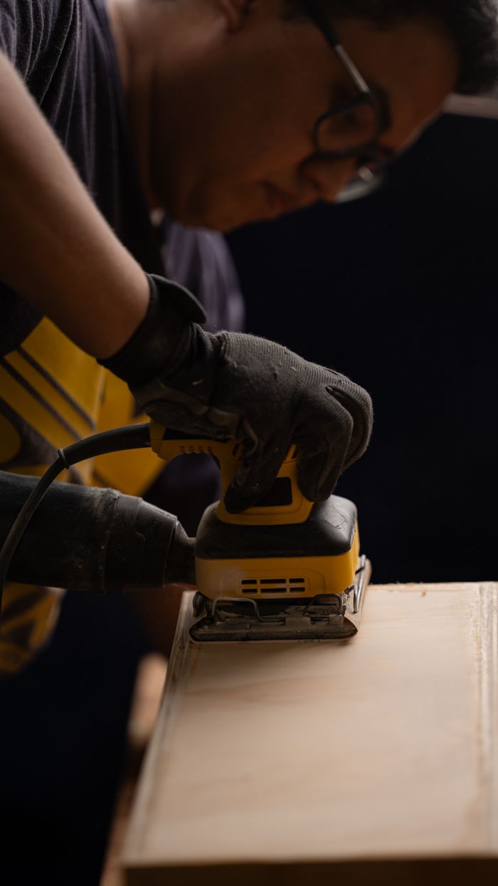 A person using an electric sander on wood, highlighting craftsmanship and woodworking skills.