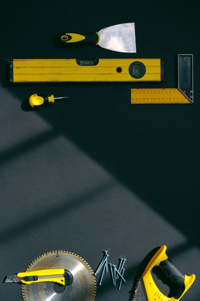 About Stylized flat lay of yellow hand tools on a dark surface with dramatic lighting.